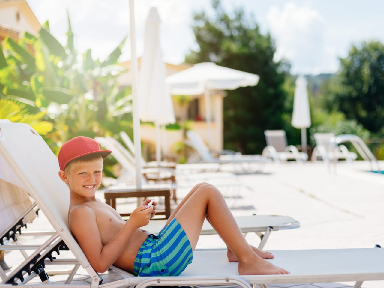 Junge in Badehose entspannt sich glücklich auf einer Sonnenliege am Pool ©iStock.com/djedzura