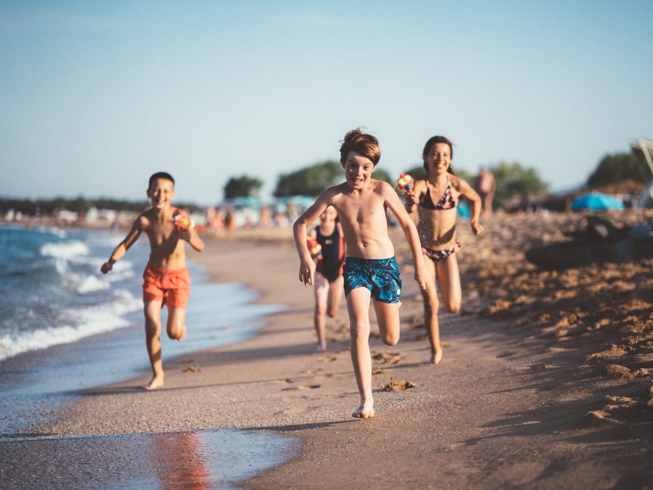 Kinder laufen und schießen mit Wasserpistolen am Strand © iStock.com/martin-dm