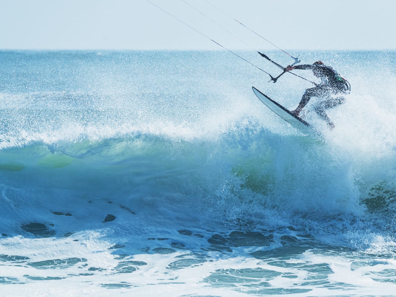 Kitesurfer springt über eine schäumende Welle © iStock.com/shaunl