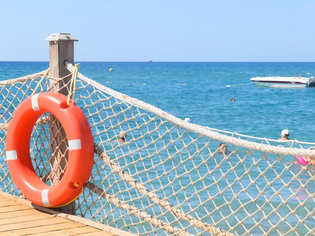 Blick von einem Steg aufs Meer. Am Steg hängt ein Rettungsring, während einige Personen im Meer schwimmen