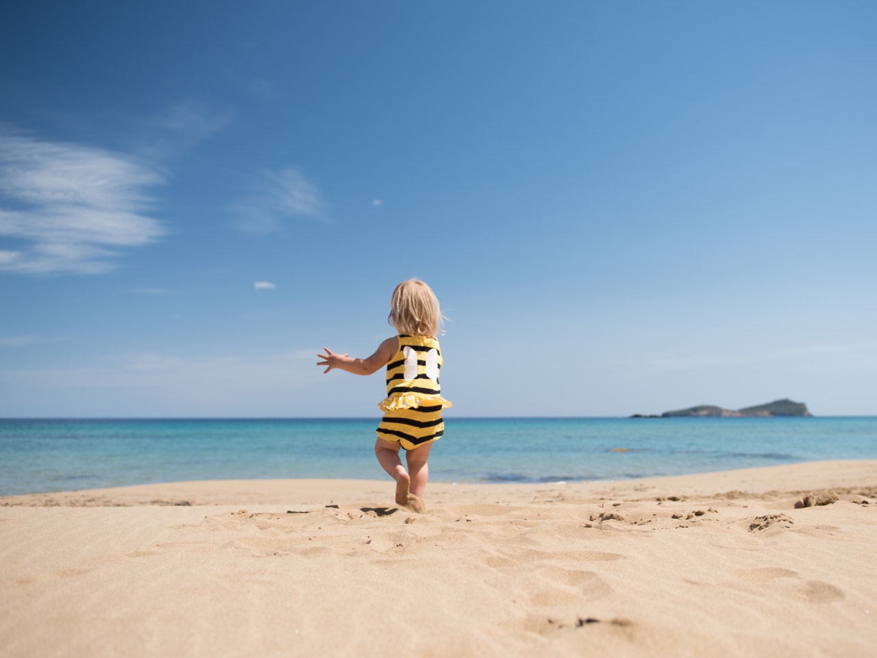 Kleines Mädchen rennt glücklich über einen Sandstrand im Urlaub © iStock.com/kamsta