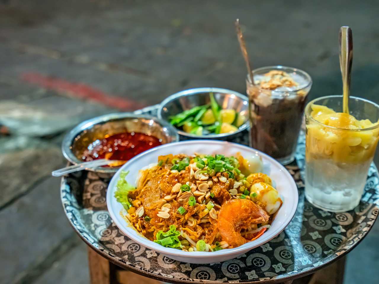 Auf einem kleinen Beistelltisch steht ein Teller vietnamesisches Mi Quảng, eine Soße und Getränke.