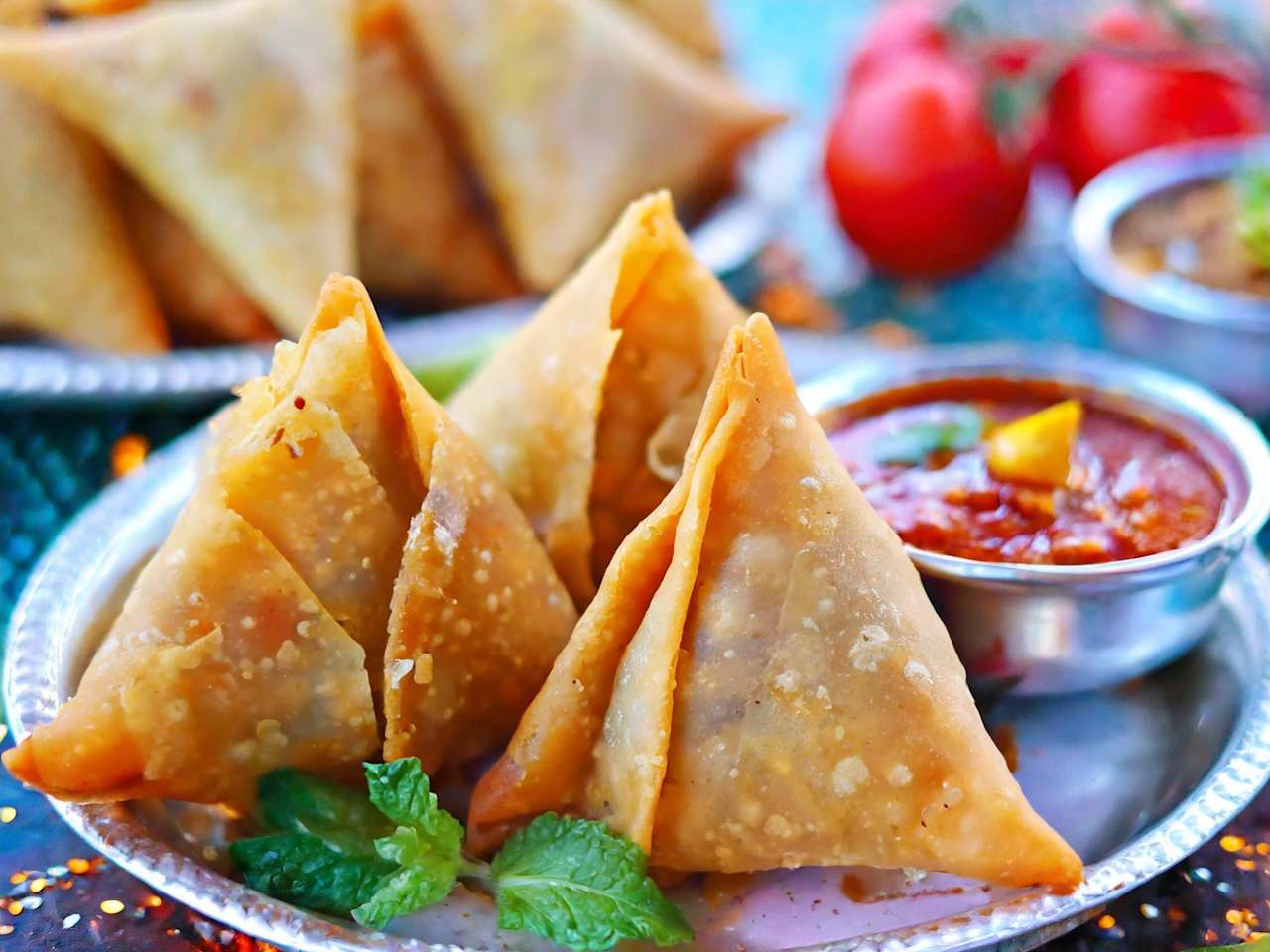 Mehrere Samosas liegen auf einem silbernen Teller mit einer kleinen Soßenschale.
