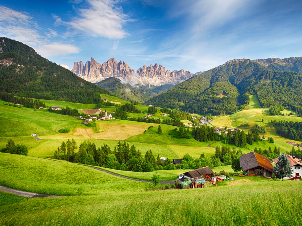 SchönesmBergpanorama mit den Dolomiten im Hintergrund und Hütten in grünem Tal © iStock.com/TomasSereda