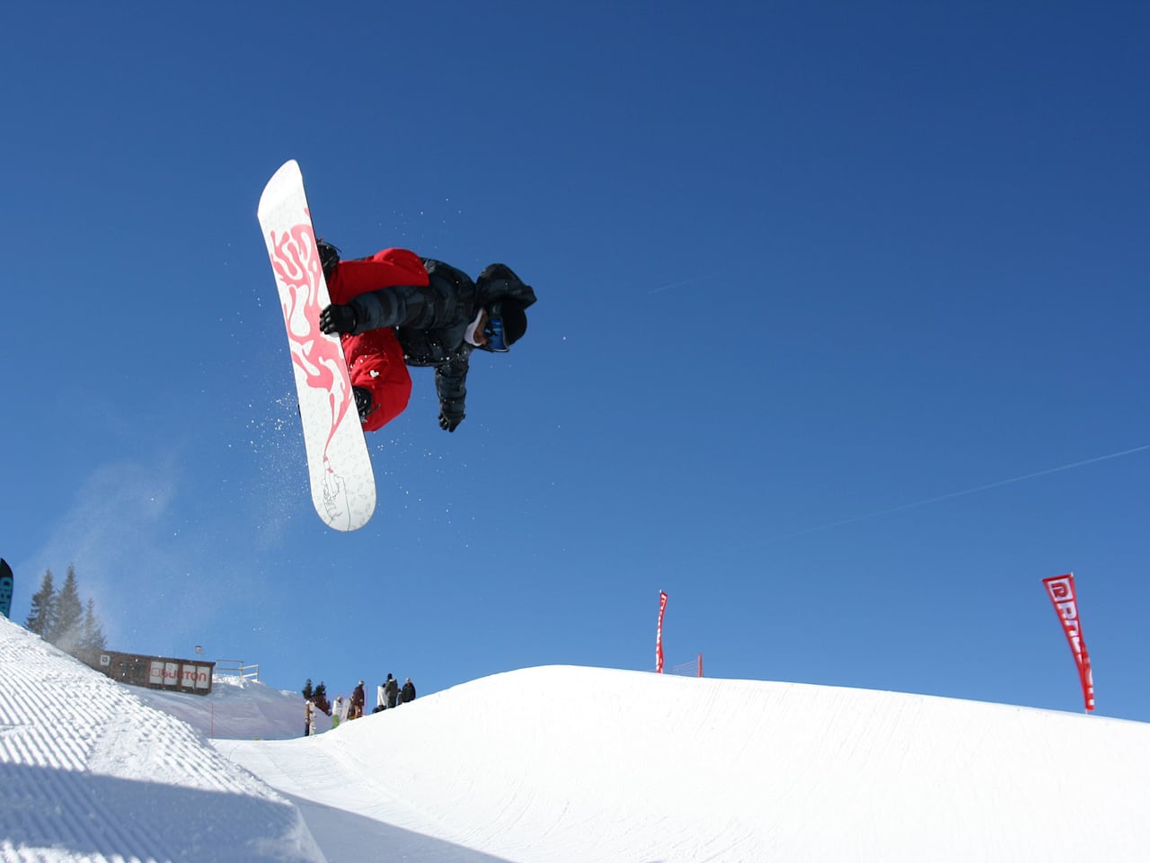 Snowboarder in der Luft beim Trick über einen Kicker im Funpark, blauer Himmel im Hintergrund, Avoriaz, Schweiz.