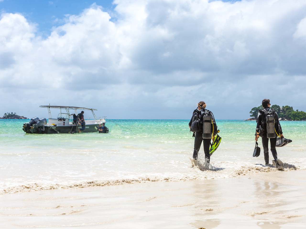 Zwei Taucher mit Ausrüstung laufen am Strand auf ein Boot zu