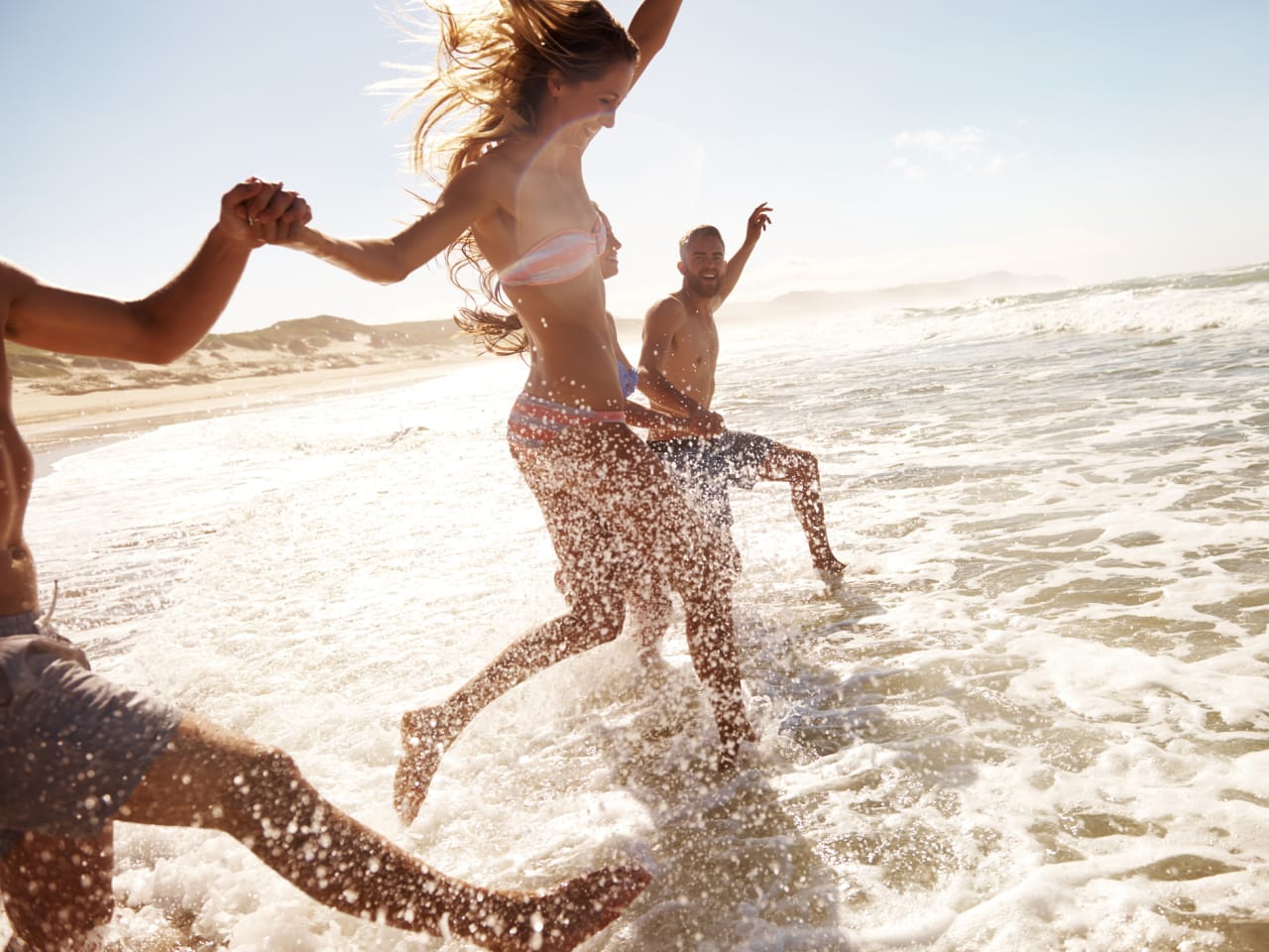 Zwei junge Paare, die am Strand durch das Wasser rennen © iStock.com/pixdeluxe
