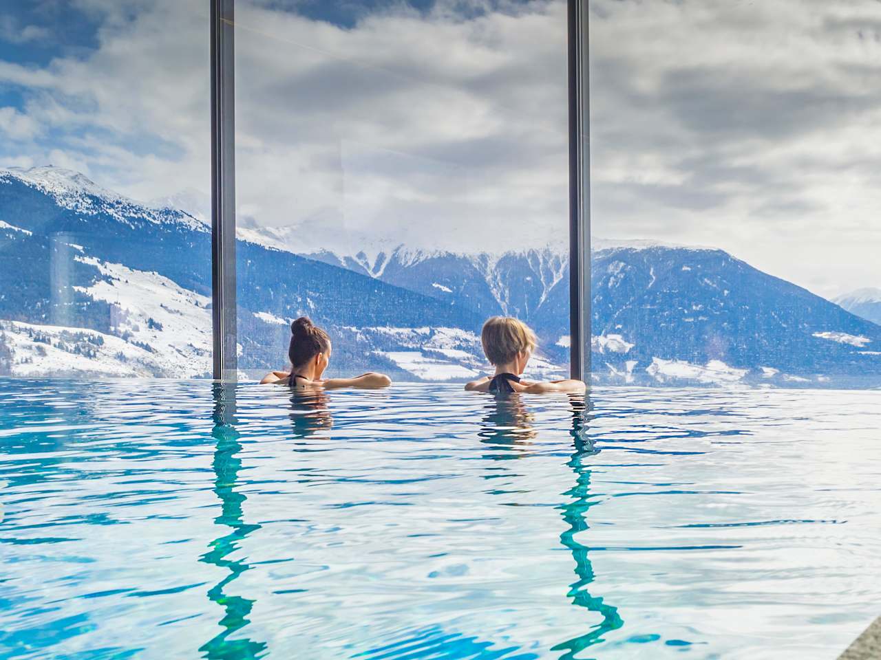 Zwei Frauen in einem Pool blicken auf eine bergige Landschaft