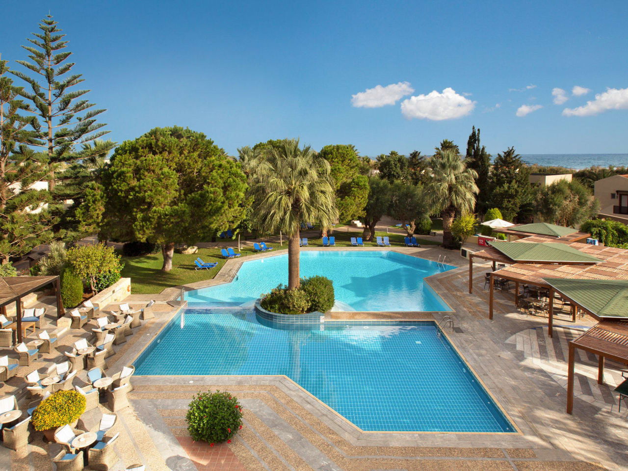 Blaues Poolbecken, Sitzmöglichkeiten, Sonnenschutz und Garten im Hotel Cretan Malia Park auf Kreta in Griechenland