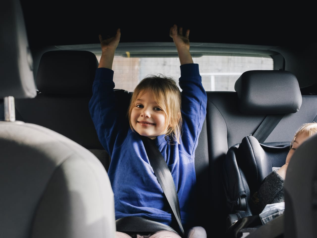 Ein kleines Mädchen sitzt fröhlich auf der Rückbank eines Autos. © Maskot/Maskot via Getty Images