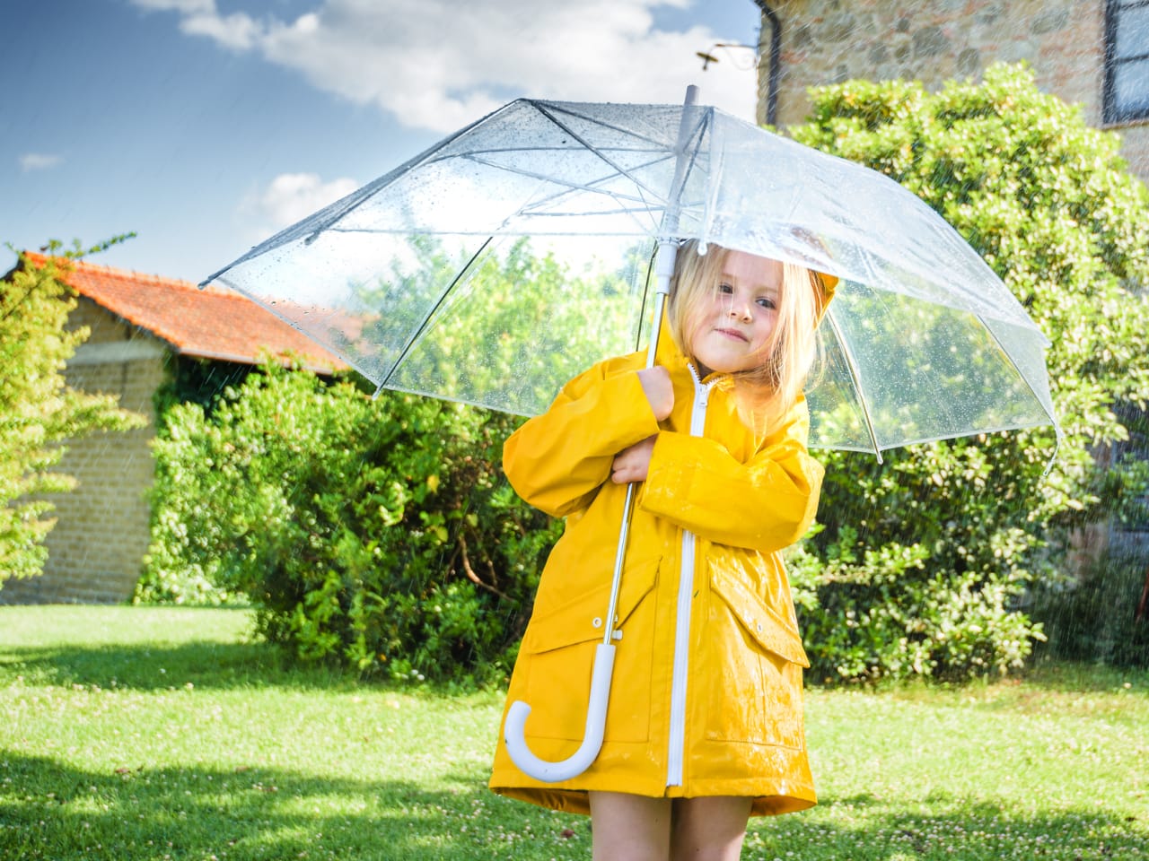 Ein Mädchen mit einem gelben Regenmantel unter einem Regenschirm.