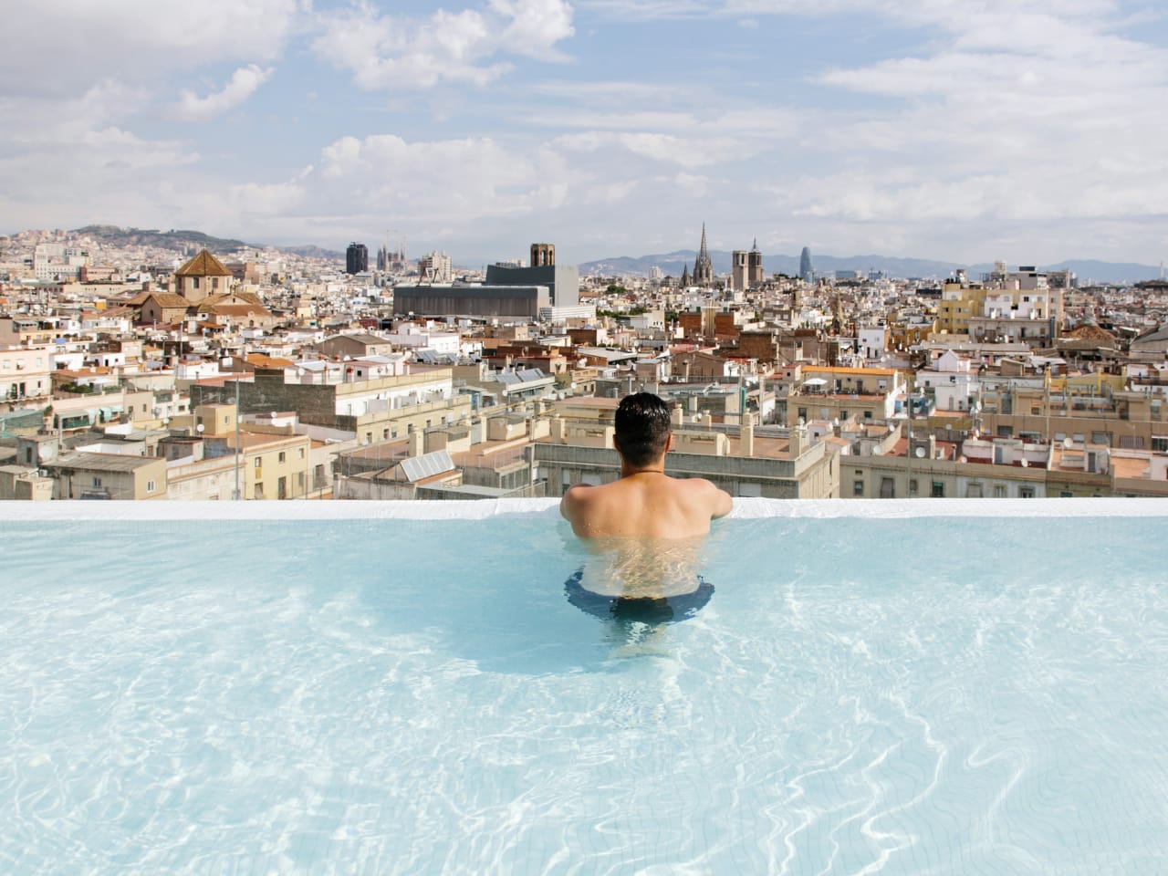 Ein Mann schaut aus einem Infinity Pool über Barcelona, Spanien.