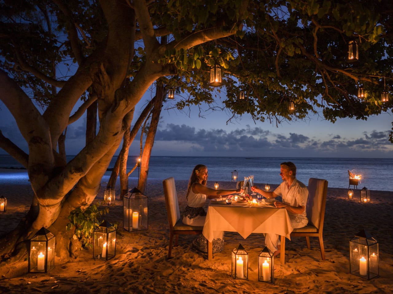 Am Strand von Mauritius, unter einem Baum, sitzt ein Paar, umgeben von Kerzen, an einem Tisch