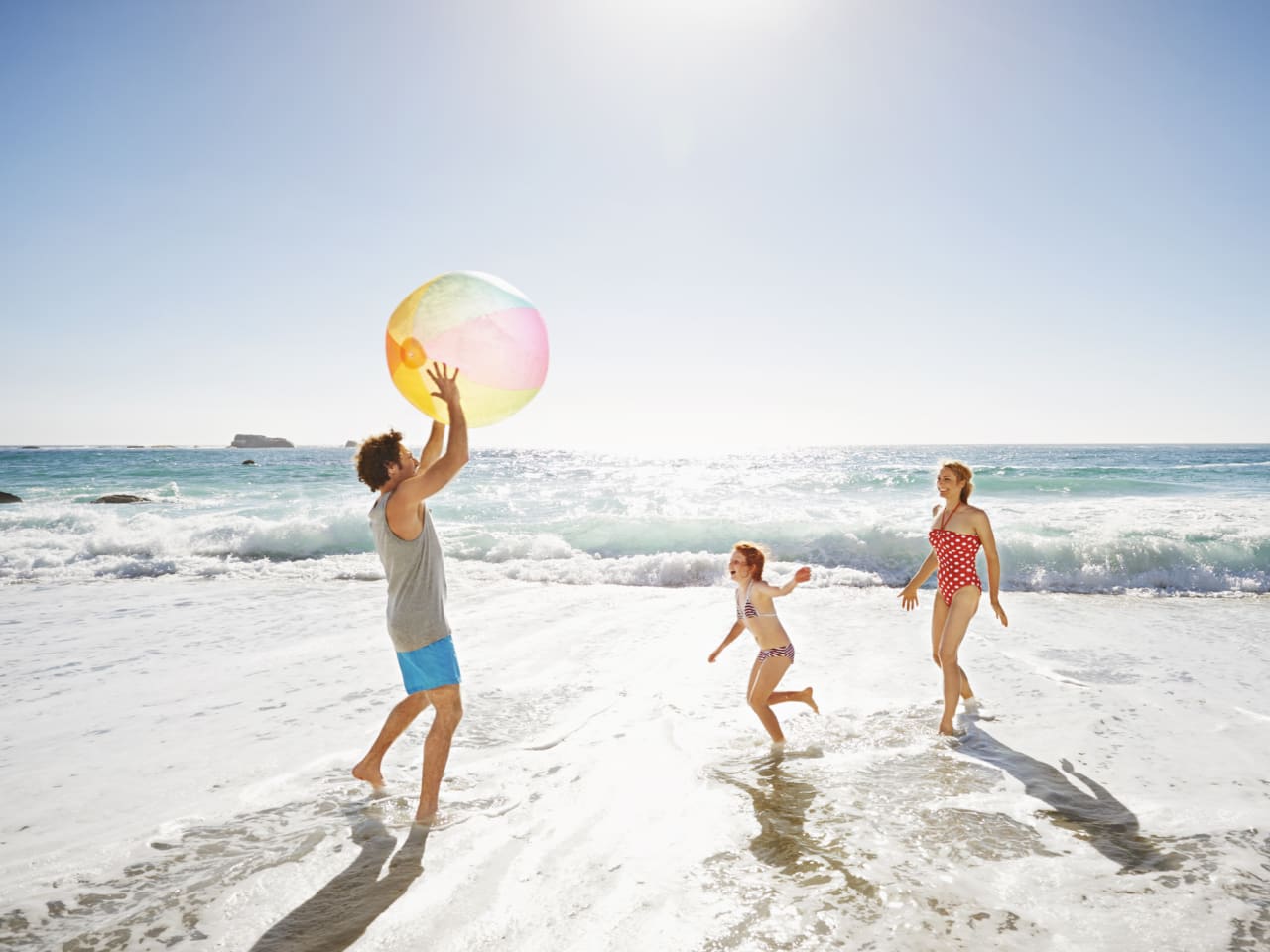 Eine Familie spielt mit einem Wasserball am Meer.