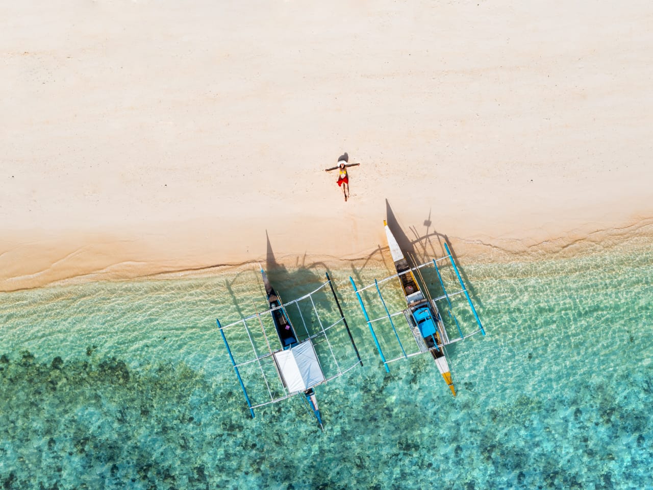 Eine Frau liegt neben zwei Booten an einem Strand auf den Philippinen. © Marco Bottigelli/Moment via Getty Images