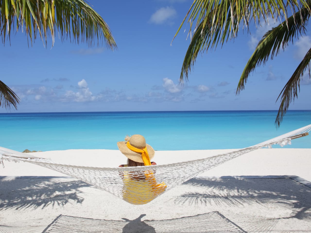 Eine Frau sitzt auf einer Hängematte an einem Paradiesstrand.