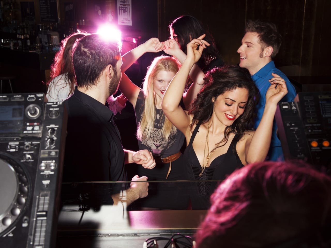 Gruppe von Freunden tanzt vor dem DJ-Pult in Nachtclub. © Manuela/Image Source via Getty Images
