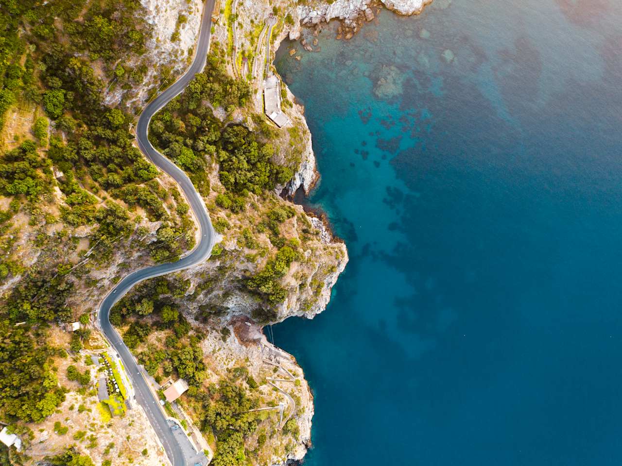 Dronenblick auf die Küstenstraße und tiefblaues Meer an der Amalfiküste, Italien. © Marco Bottigelli via Getty Images