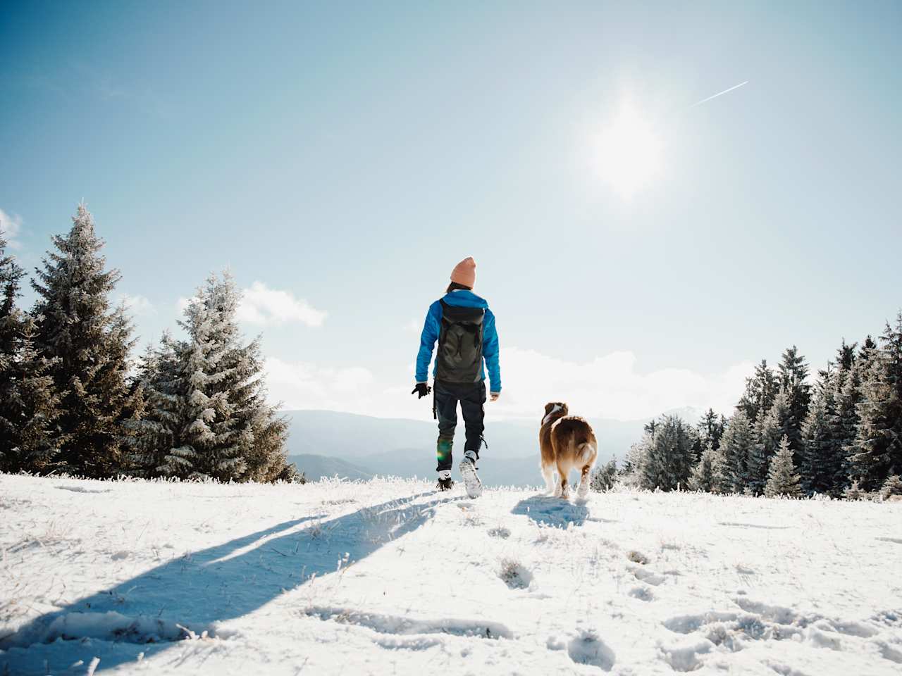 Eine Frau wandert mit ihrem Hund in einer verschneiten Landschaft.