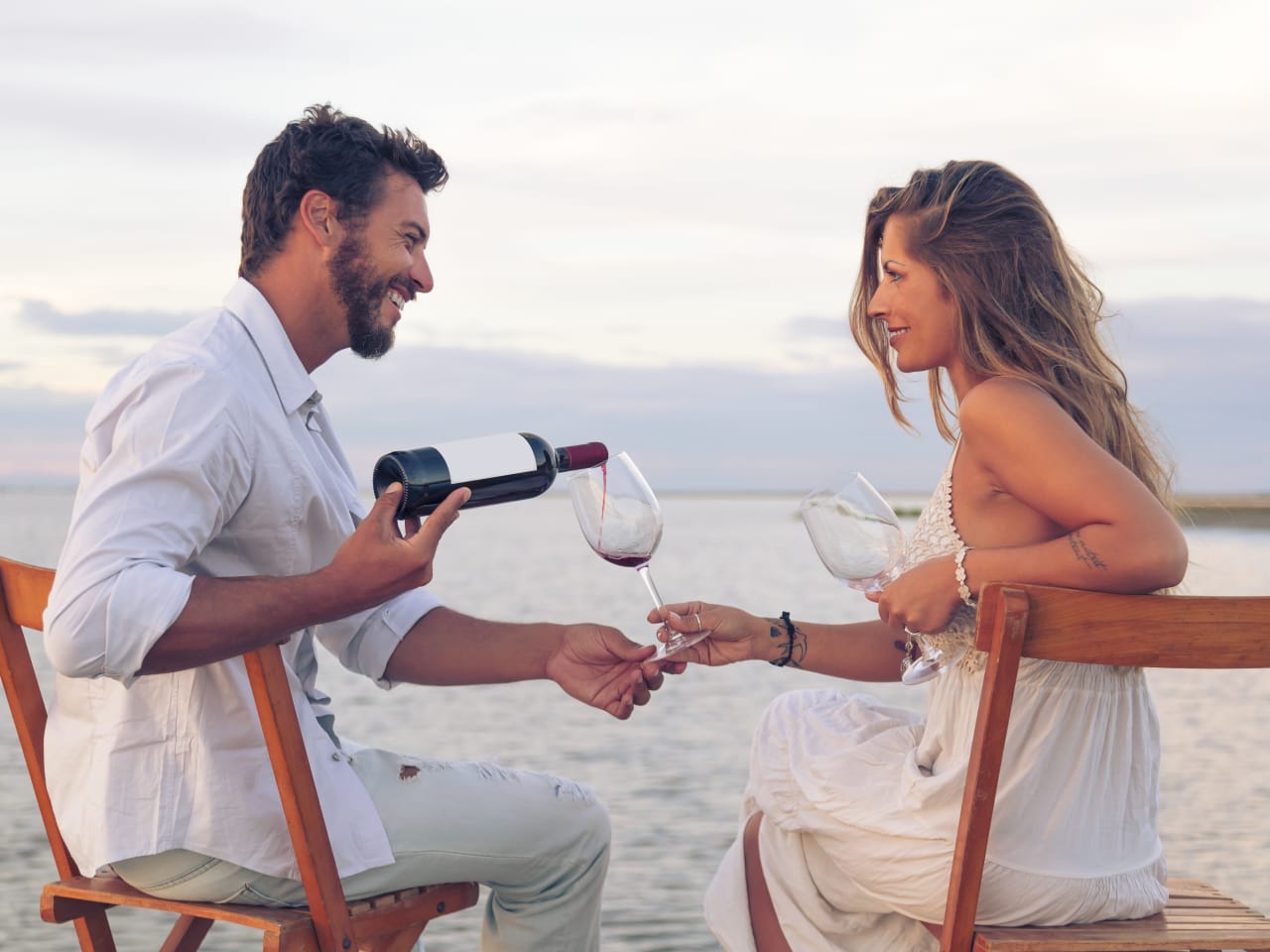 Paar am Strand, Mann gießt Wein in ein Glas ein in Griechenland