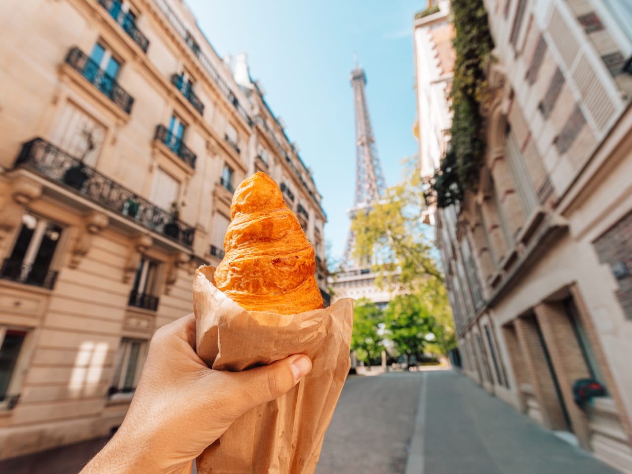 Eine Person mit einem Croissant vor dem Eiffelturm in Paris, Frankreich © Alexander Spatari/Moment via Getty Images