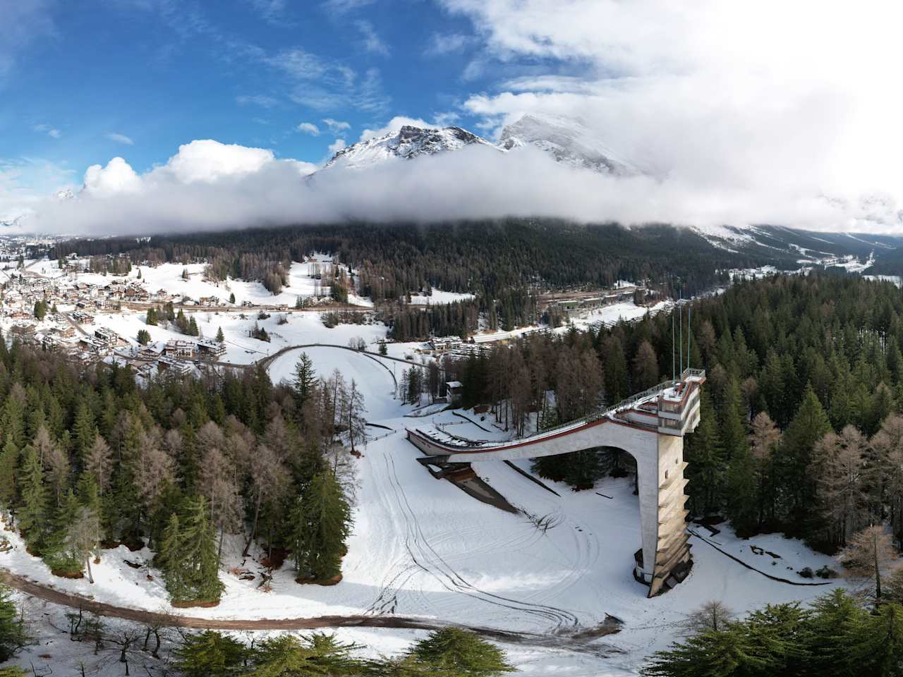Luftaufnahme mit Blick auf eine alte Sprungschanze in einem bewaldeten Gebiet in den Alpen.