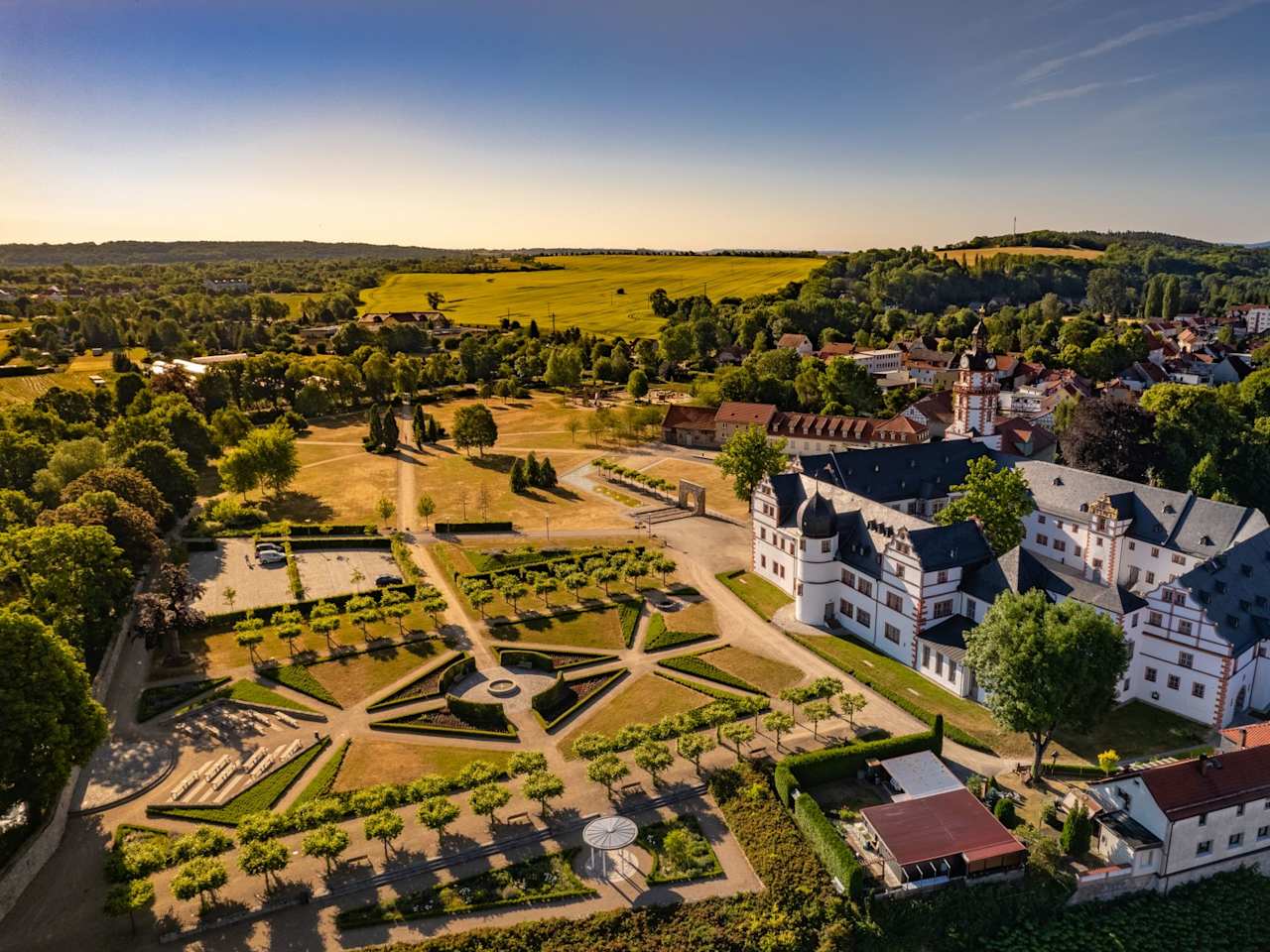 Luftperspektive auf ein Schloss am Rande einer Stadt, welches an einen großen, geometrischen Garten angrenzt.