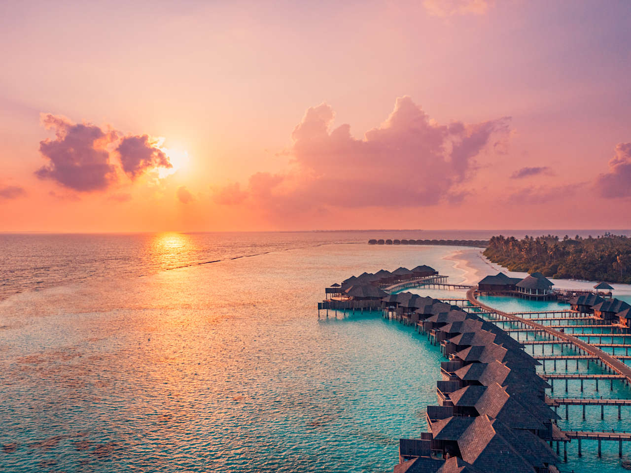 Sonnenuntergang im Meer neben Wasservillen und Holzsteg, Malediven. © Levente Bodo via Getty Images