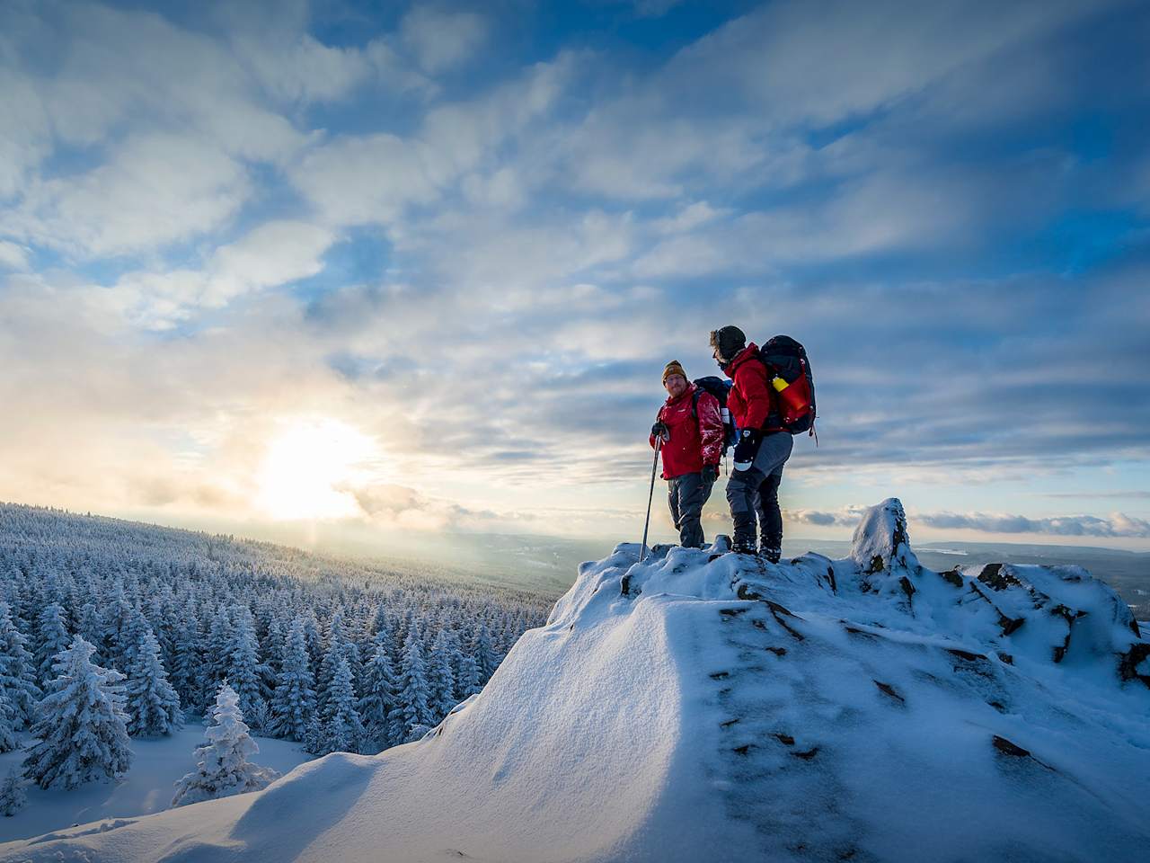 Zwei Wanderer stehen auf einem schneebedeckten Gipfel.