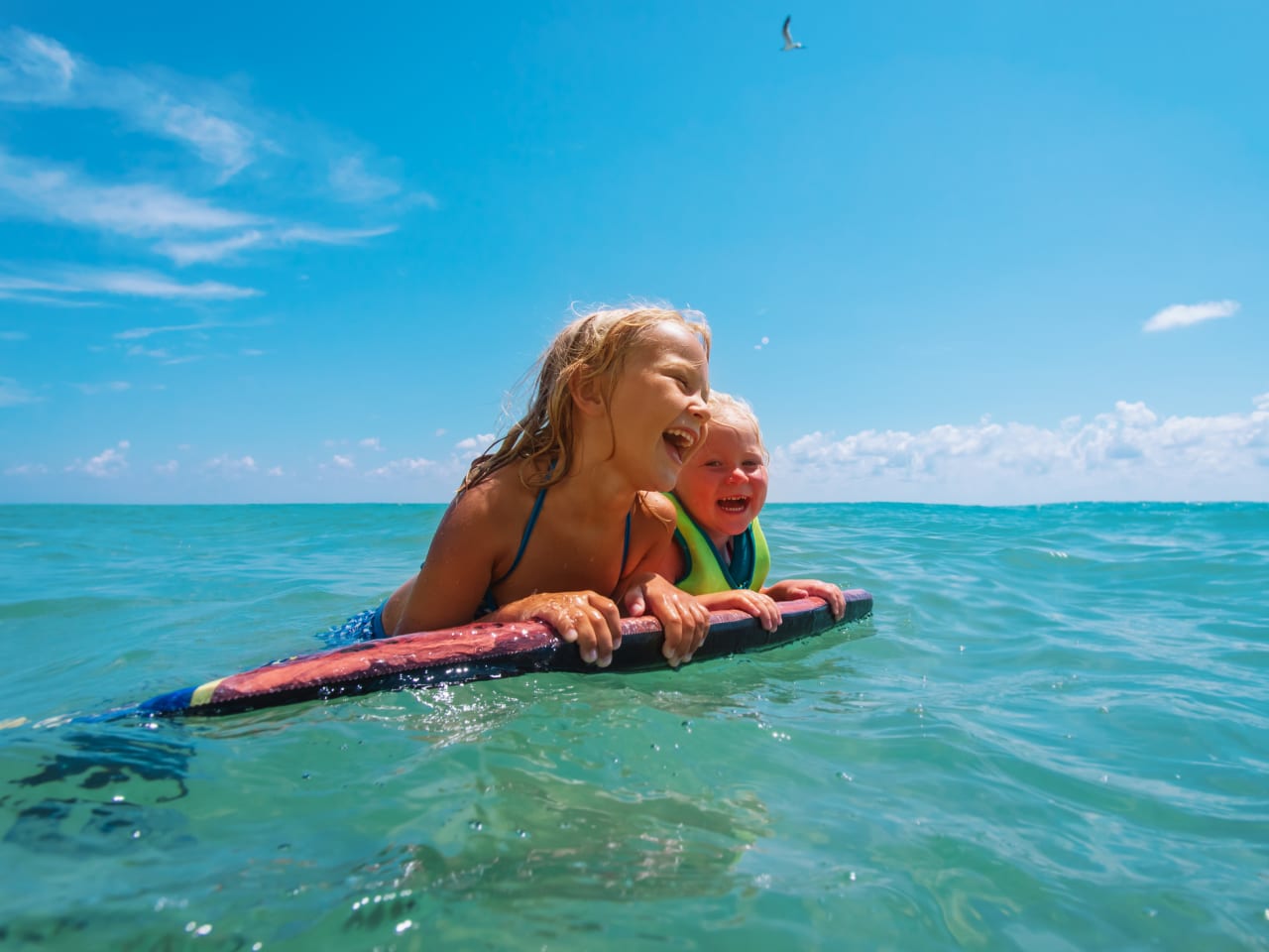 Zwei Kinder schwimmen mit einem Schwimmbrett im Meer.