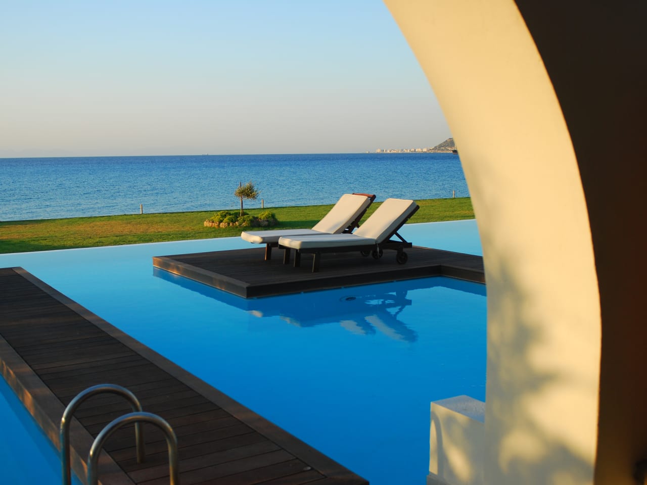 Zwei Sonnenliegen an einem Pool mit Meerblick auf Rhodos, Griechenland.