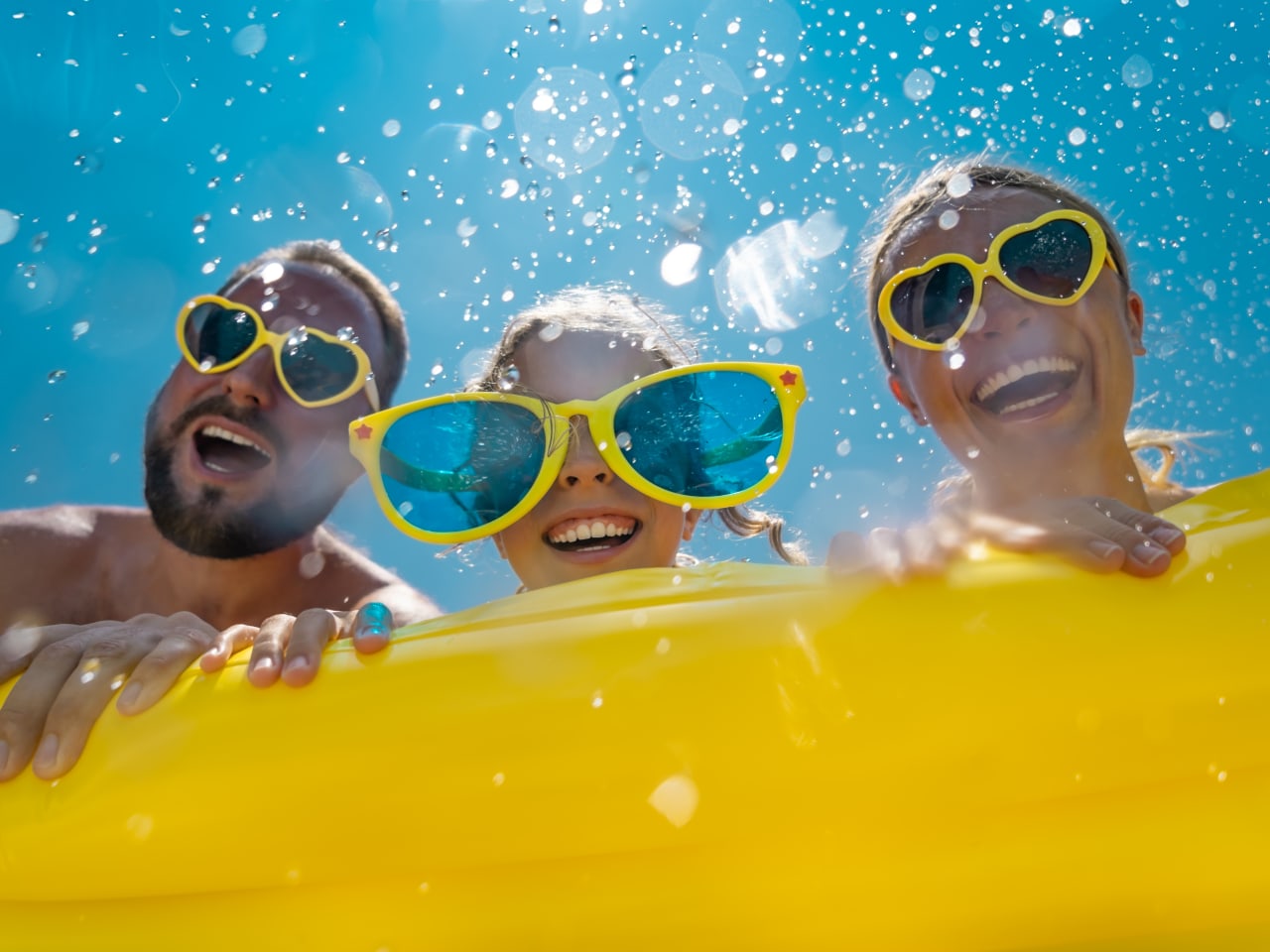 Familie hat Spaß im Wasser, alle tragen gelbe Sonnenbrillen.