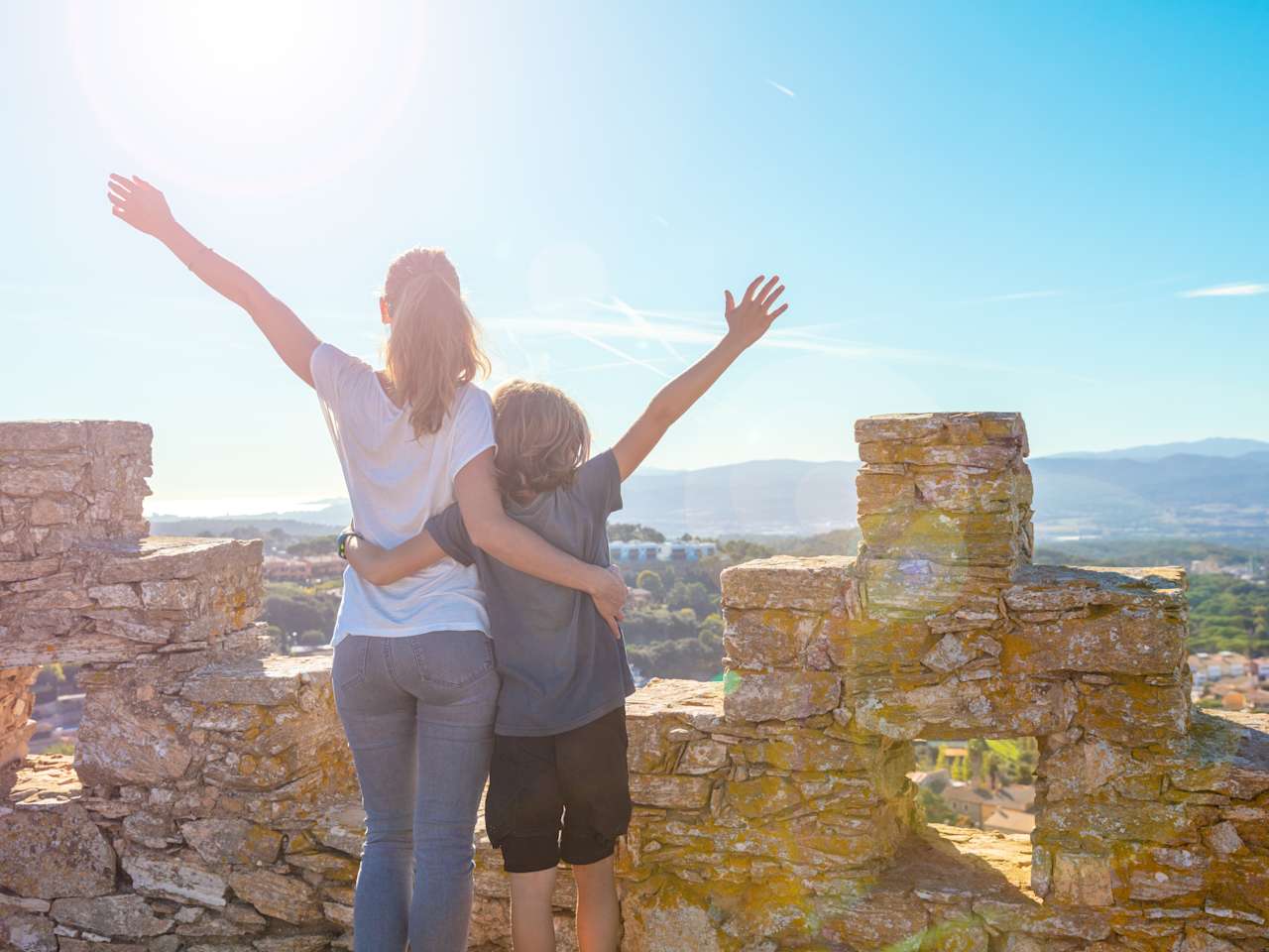 Frau und Kind umarmen sich und schauen von einer Burg auf die Costa Brava, Spanien