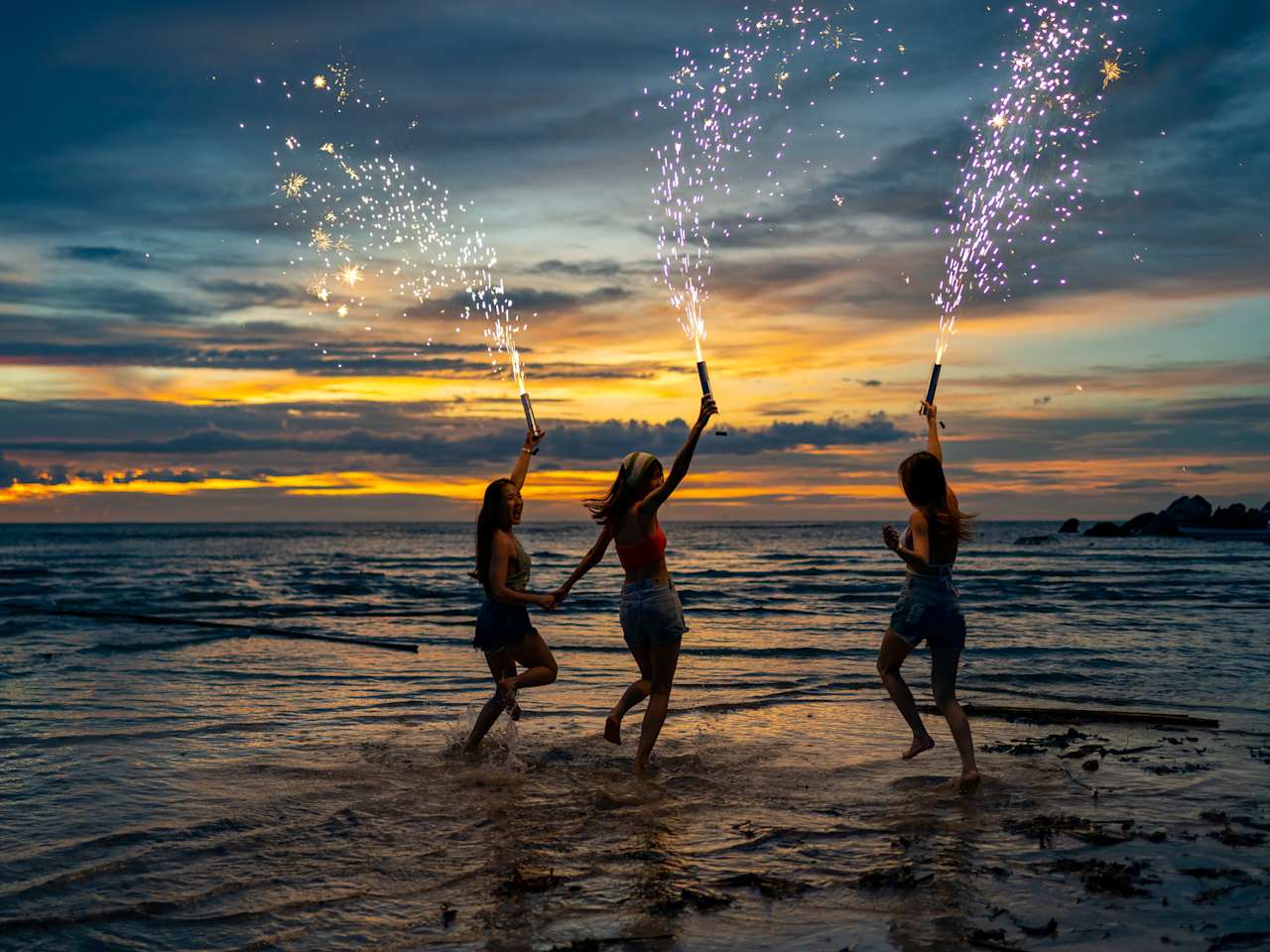 Drei Frauen springen ins Meer mit Silvesterfontänen und haben Spaß