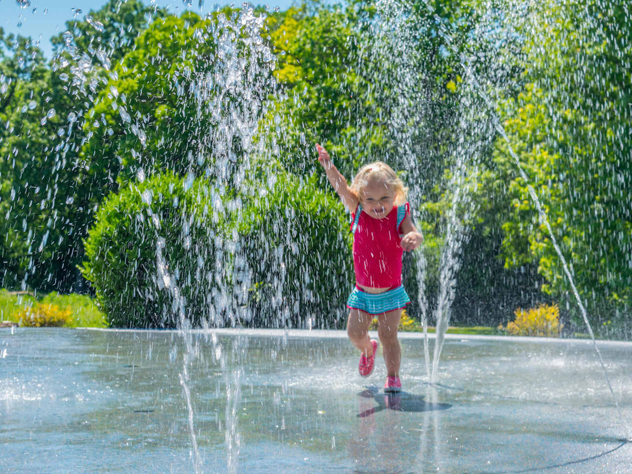 Kleines Mädchen läuft fröhlich durch einen Wasserbrunnen im Sommer.