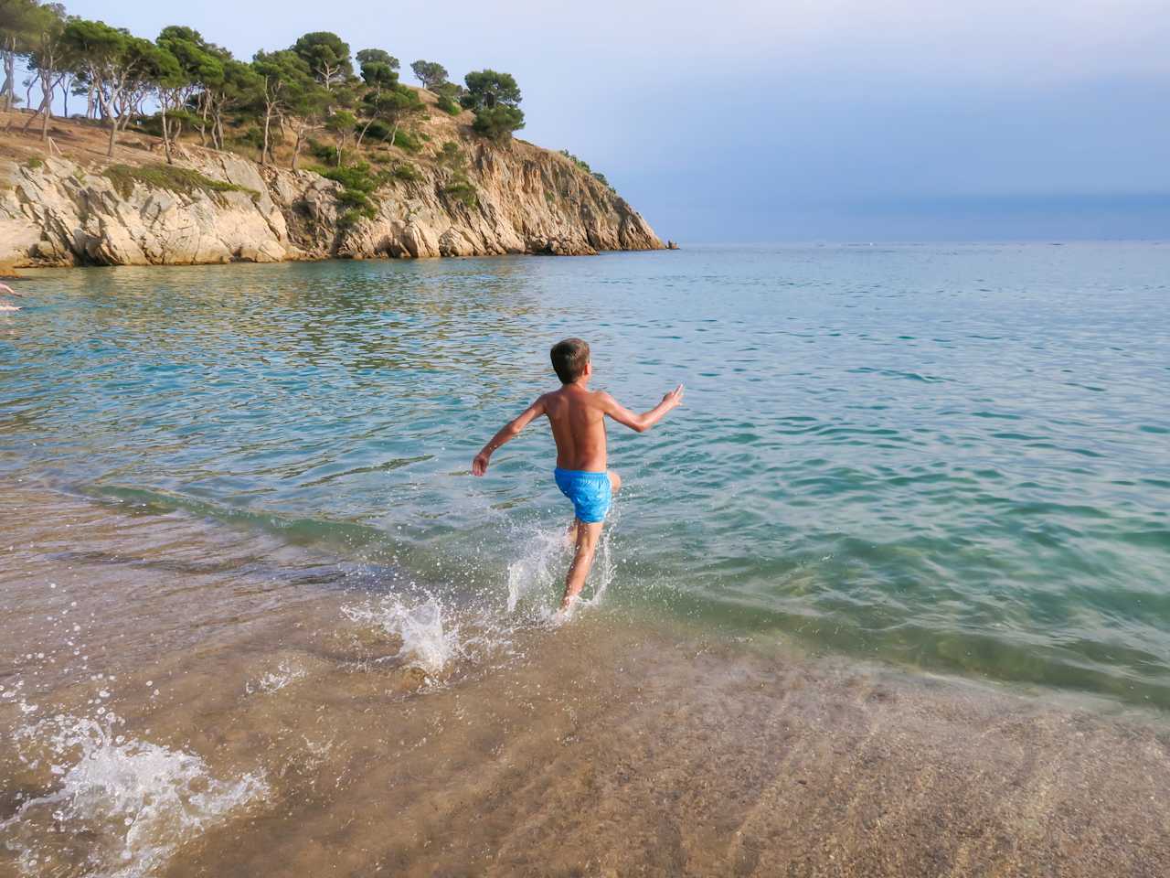 Kind läuft am Strand ins Meer an der Costa Brava, Spanien.