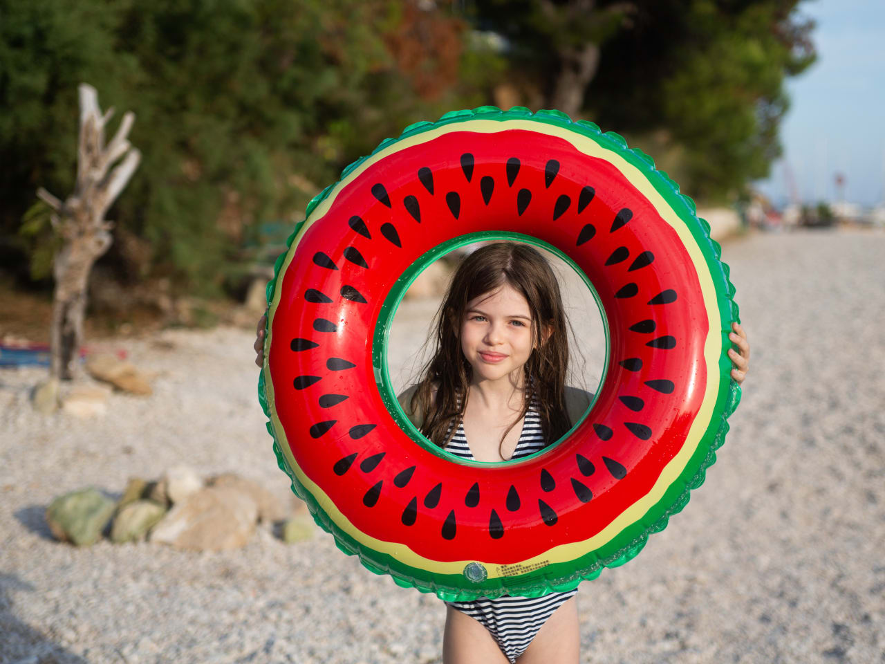 Mädchen hält einen Schwimmring in Melonen-Optik an einem Strand in Kroatien hoch.