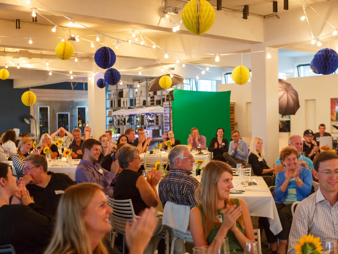 Gäste sitzen an ihren Tischen und applaudieren beim Community Event 2017