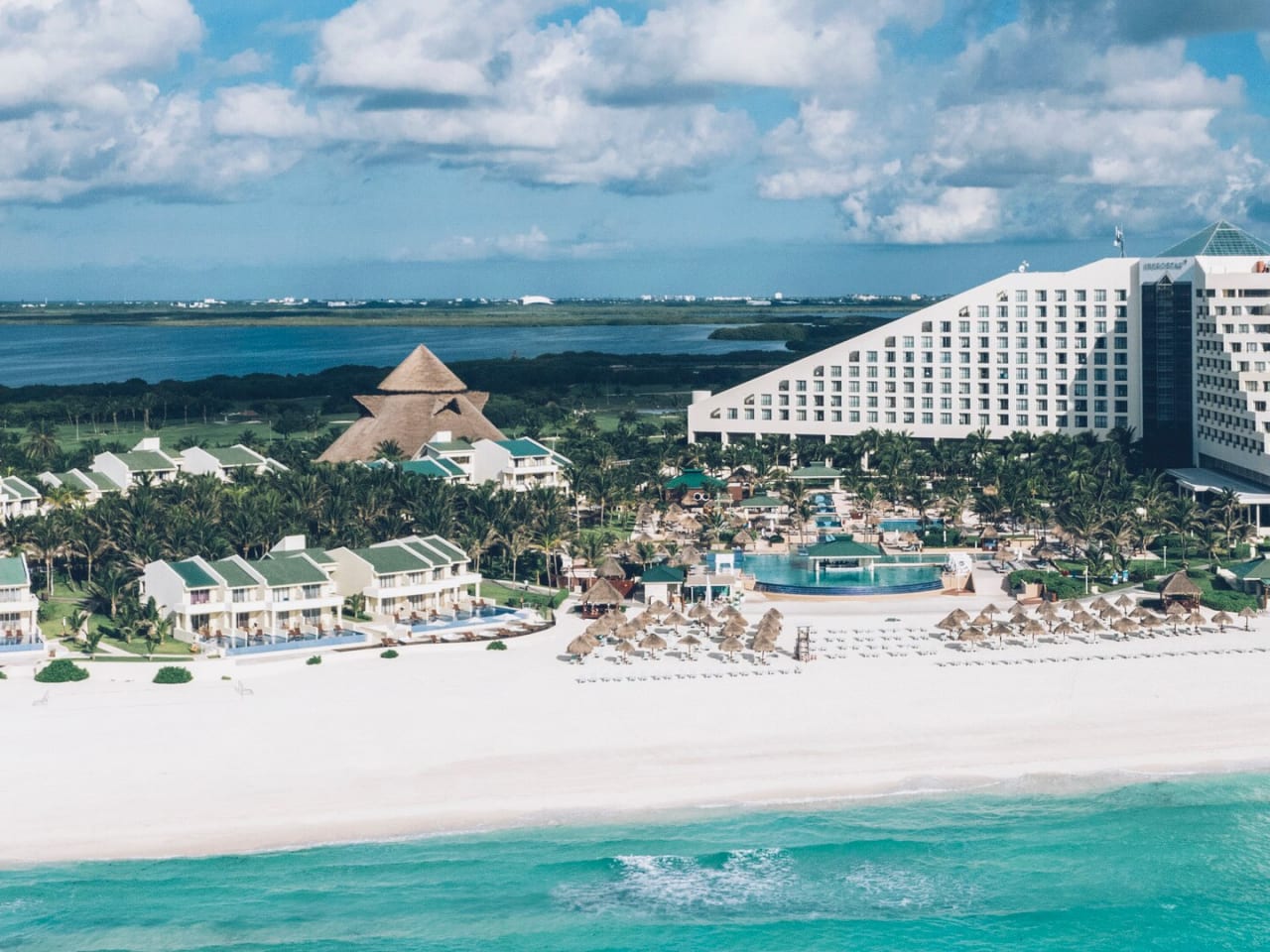 Luftaufnahme der Hotelanlage mit Strand, Grünanlagen und dem pyramidenartigen, weißen Hotelgebäude