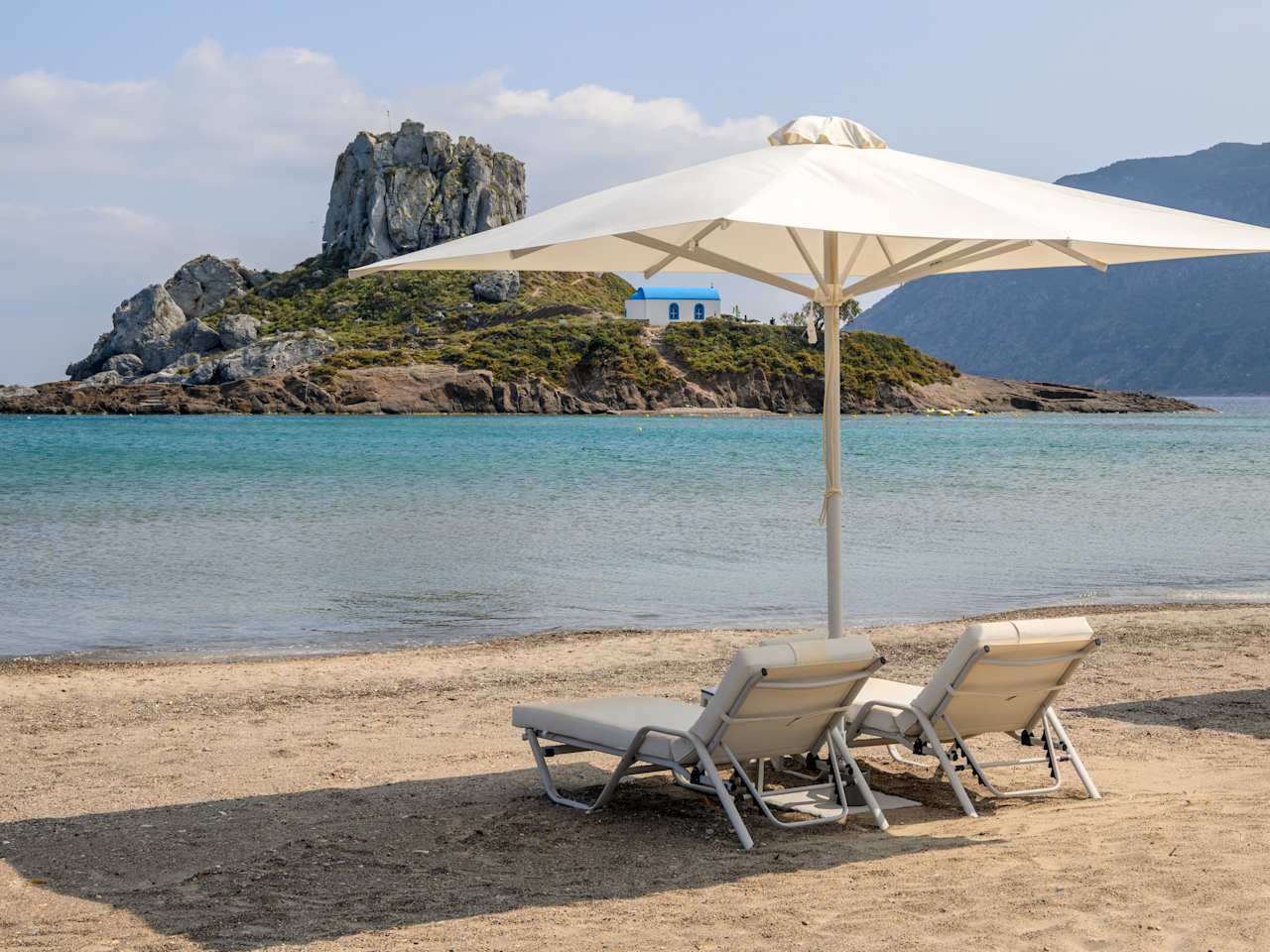 Strand Agios Stefanos mit zwei Liegen und Sonnenschirm auf Kos, Griechenland.