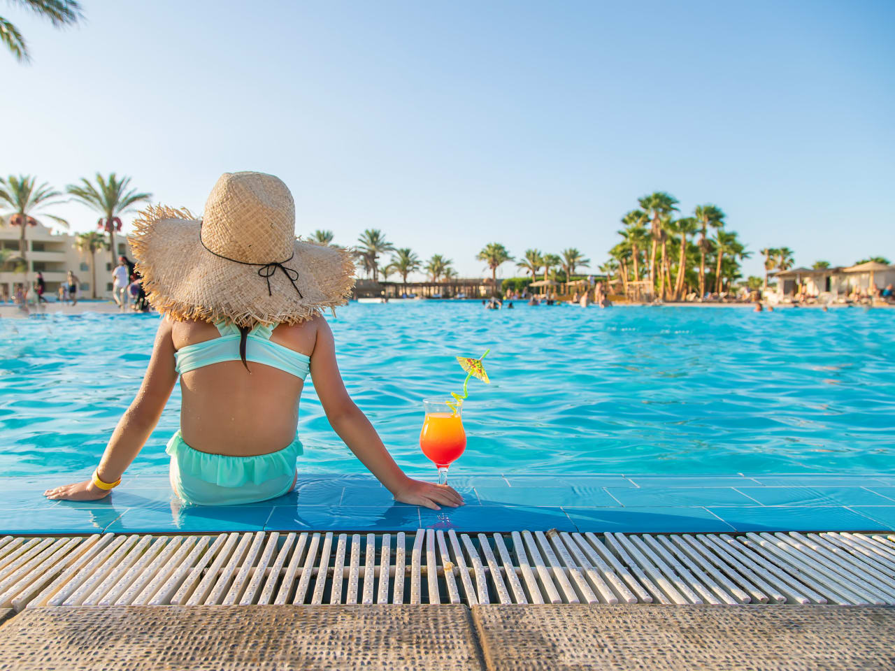 Kind sitzt am Pool mit Sonnenhut und schaut auf eine Hotelanlage in Ägypten, wo es seine Ferien verbringt