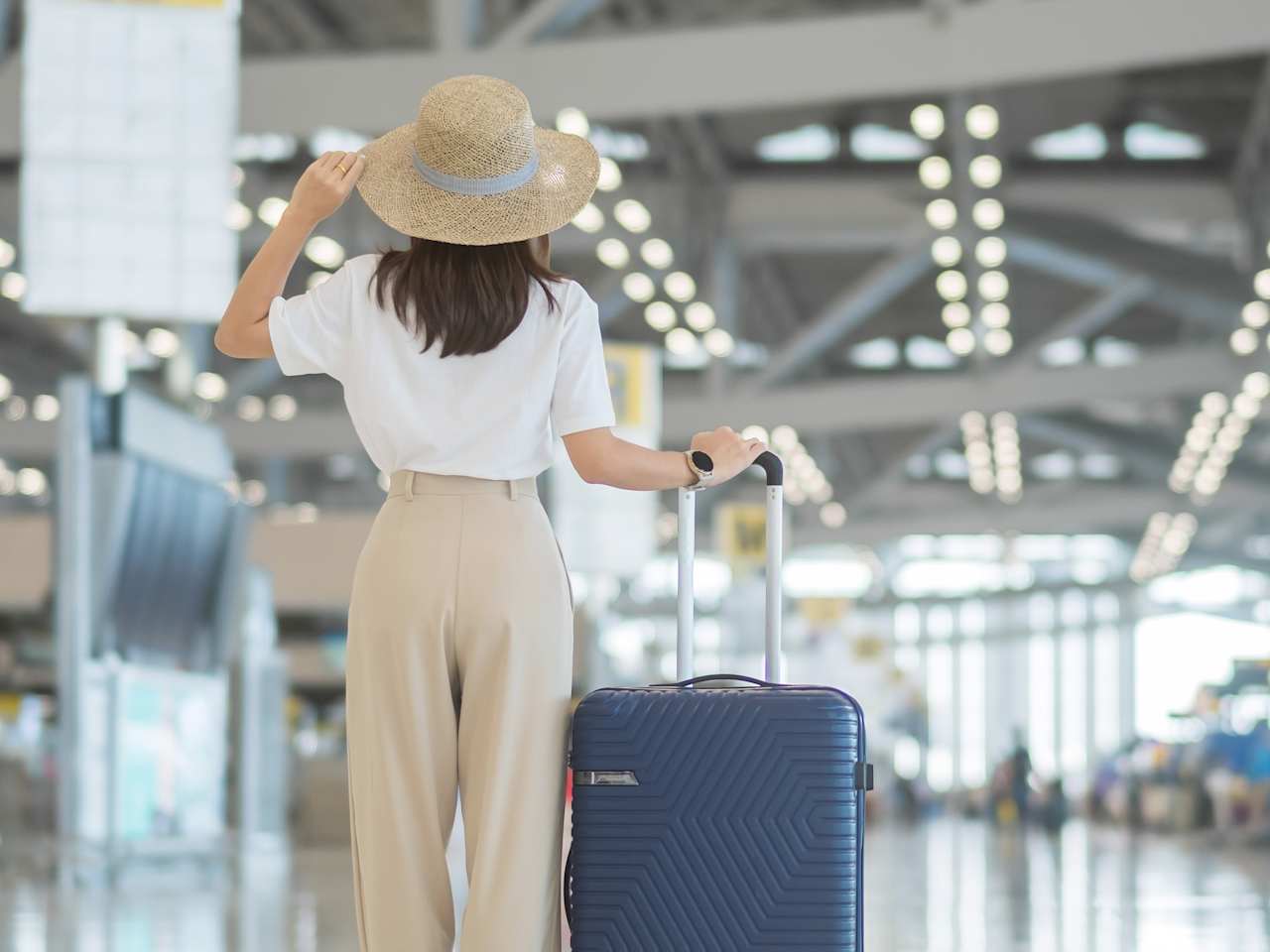 Frau steht mit Sonnenhut am Flughafen © Shutterstock