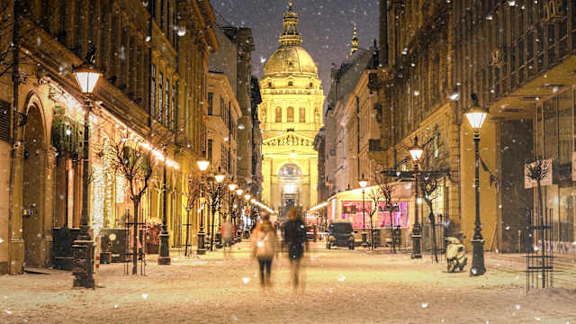 Beleuchtete Stadtbild Zrinyi Strasse in Budapest mit St Stephen Basilika in einer verschneiten Winterlandschaft in der Abenddämmerung. © _ultraforma_ via Getty Images
