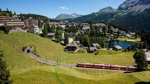 Eine Stadt liegt in den Bergen an einem See. Ein Zug fährt auf die Stadt zu.