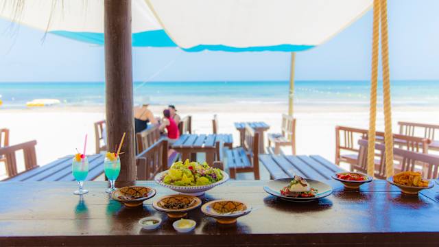 Blick auf Speisen, die auf der Theke einer Strandbar stehen Dahinter erstreckt sich der Strand und das Meer