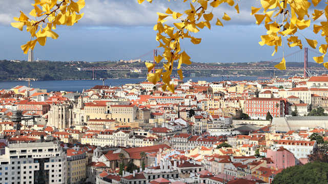 Blick auf die Häuser von Lissabon und eine Brücke übers Wasser im Hintergrund.