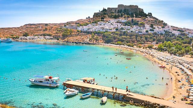 Blick auf die Bucht von Lindos mit Ausflugsbooten und Menschen am Strand, Rhodos, Griechenland.