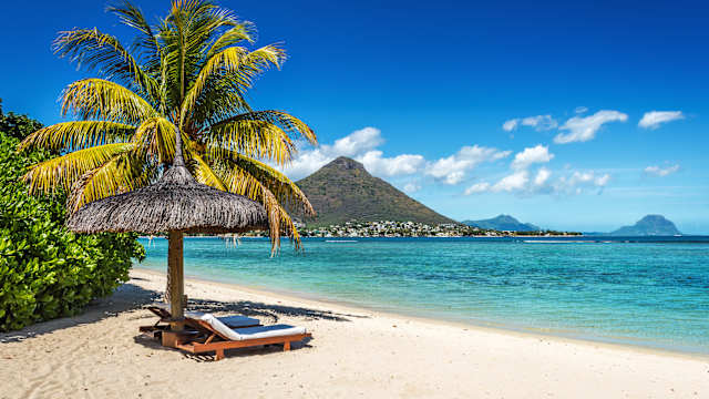 Eine Liege unter einem Sonnenschirm an einem Strand.