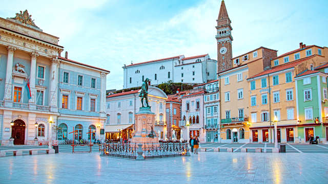 Ein Marktplatz im Morgenlicht. In der Mitte steht eine Statue.