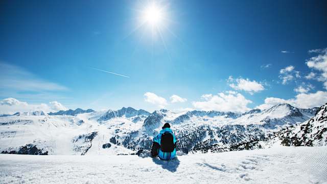 Snowboarder sitzt am Rand des Berges und überblickt die Winterlandschaft in Andorra. © aleksle via Getty Images
